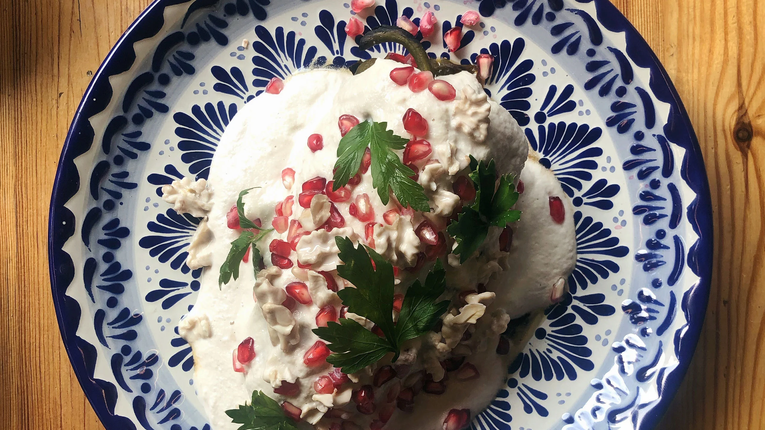 Plato de chile en nogada poblano servido en talavera, cubierto con nogada blanca, granada roja y hojas de perejil, representando los colores de la bandera de México.