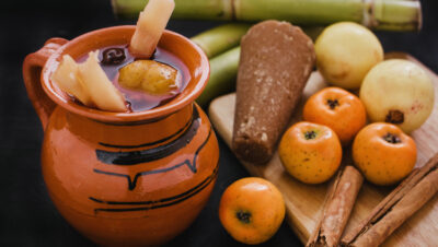 Ponche navideño: jarro de barro con ponche, tejocotes, manzanas y caña de azúcar