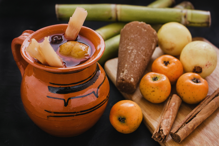 Ponche navideño: jarro de barro con ponche, tejocotes, manzanas y caña de azúcar